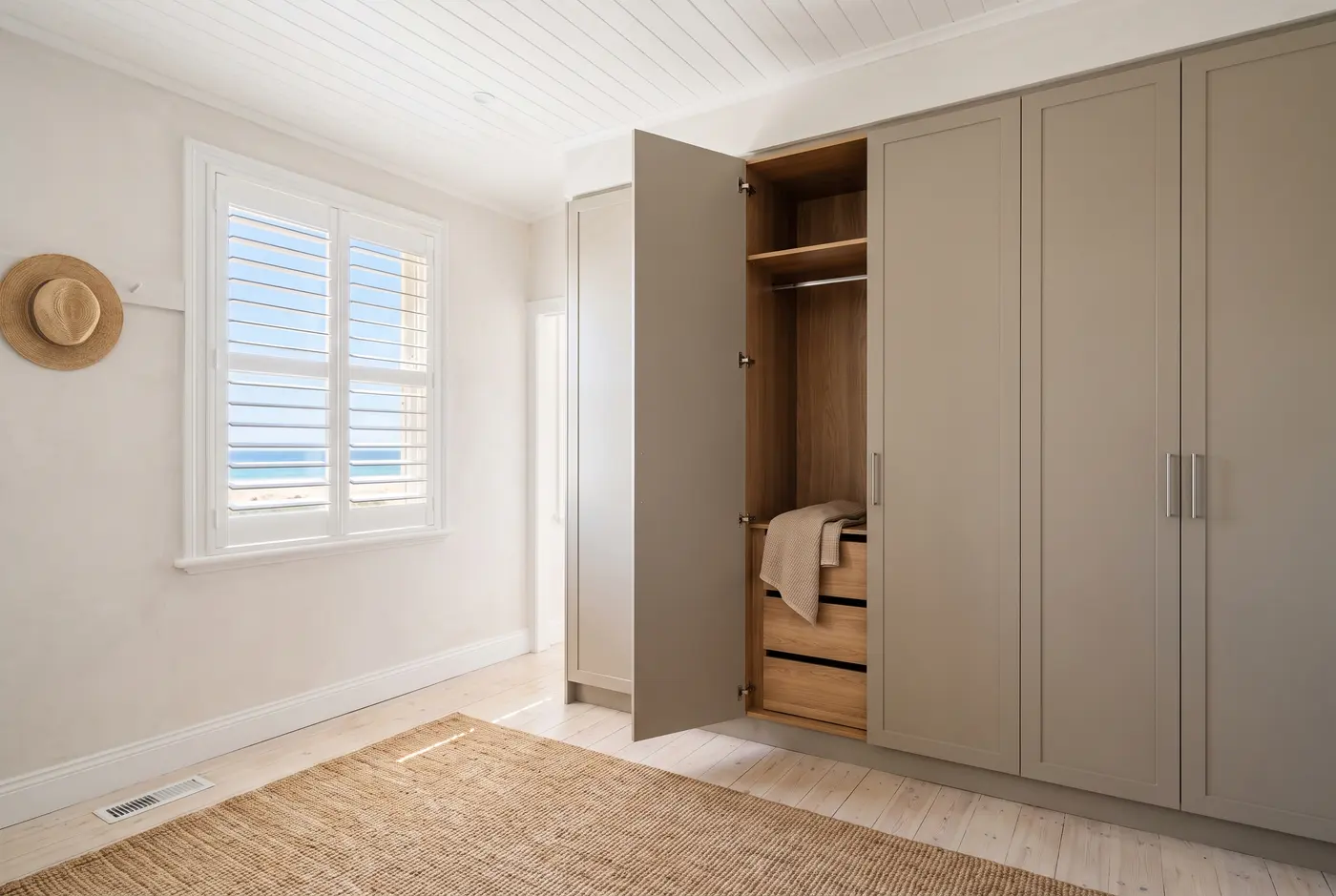A compact built-in wardrobe with sealed, salt-air-aware finishes in a light, airy Henley Beach coastal cottage bedroom